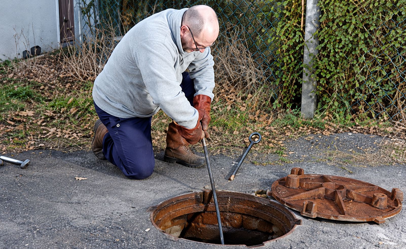 Homme agenouillé près d'une bouche d'égout ouverte pour un curage
